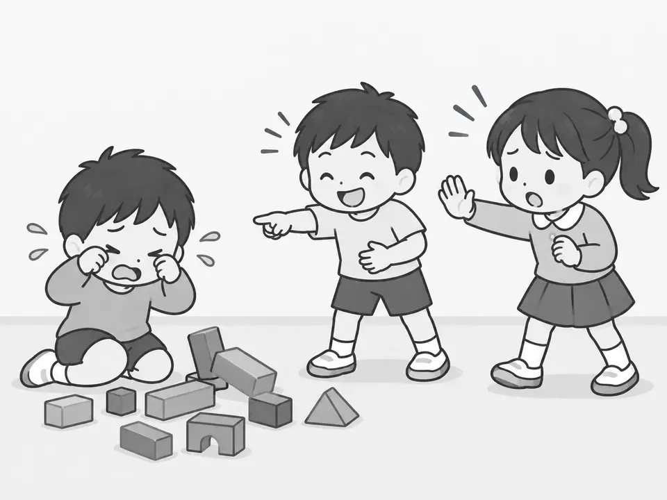 左の男の子が崩れた積み木の前で泣いています。中央の男の子が指を向けて笑い、右の女の子が止めるように手を上げています。